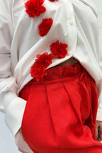 White blouse with red floral embellishments and red pants on a white background