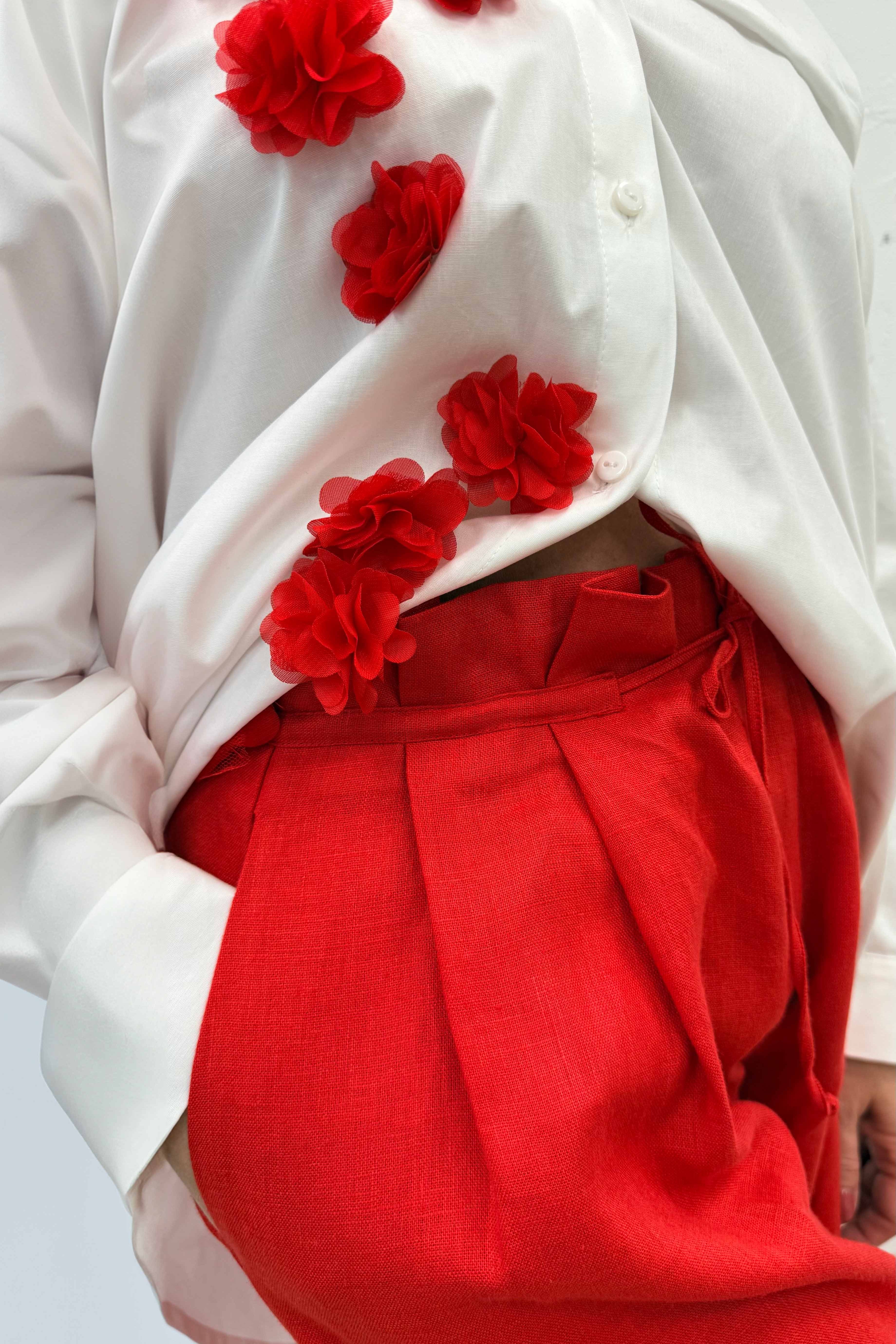 White blouse with red floral embellishments and red pants on a white background