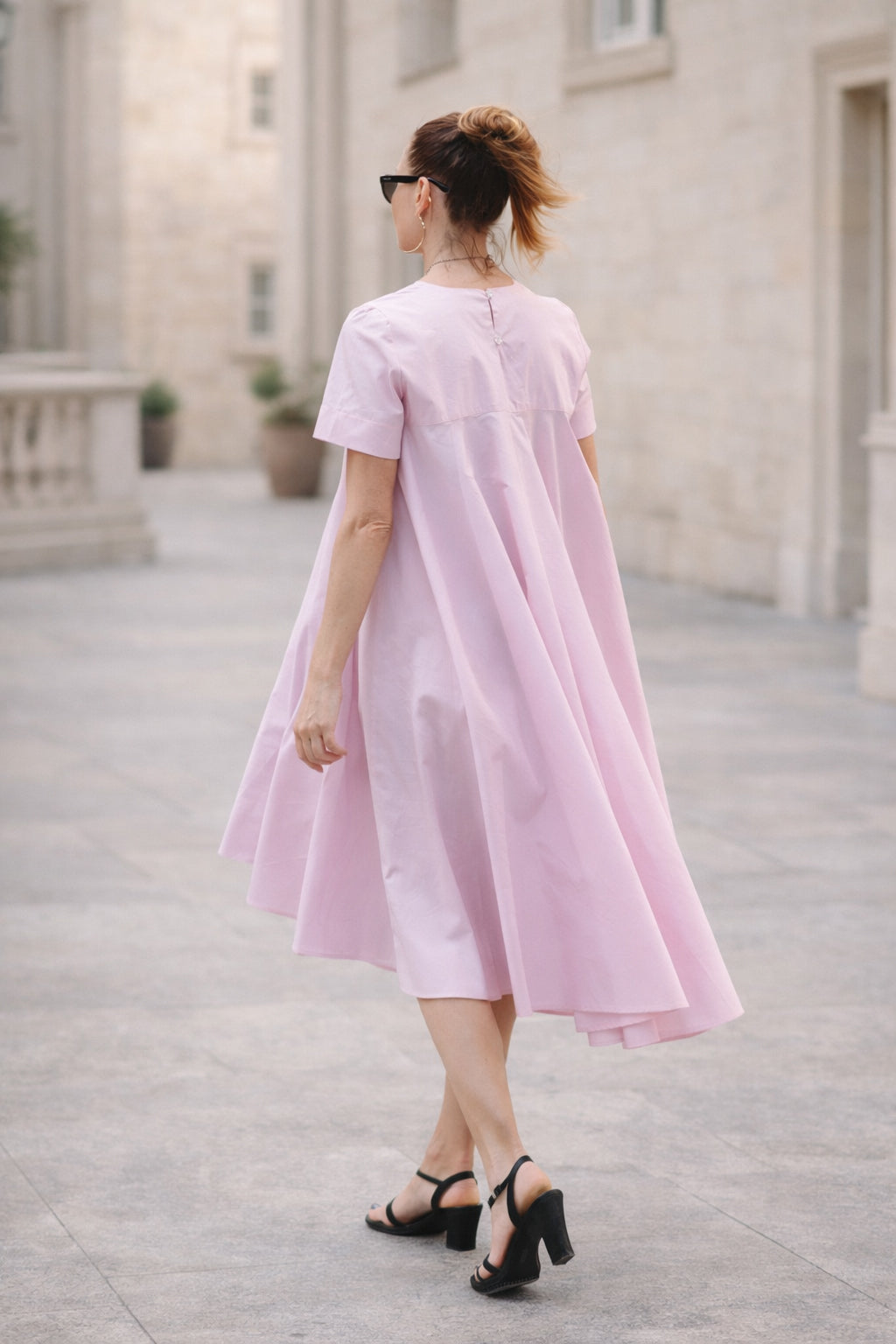 Woman wearing a pink dress standing on a stone pavement with a building in the background