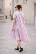 Woman wearing a pink dress standing on a stone pavement with a building in the background