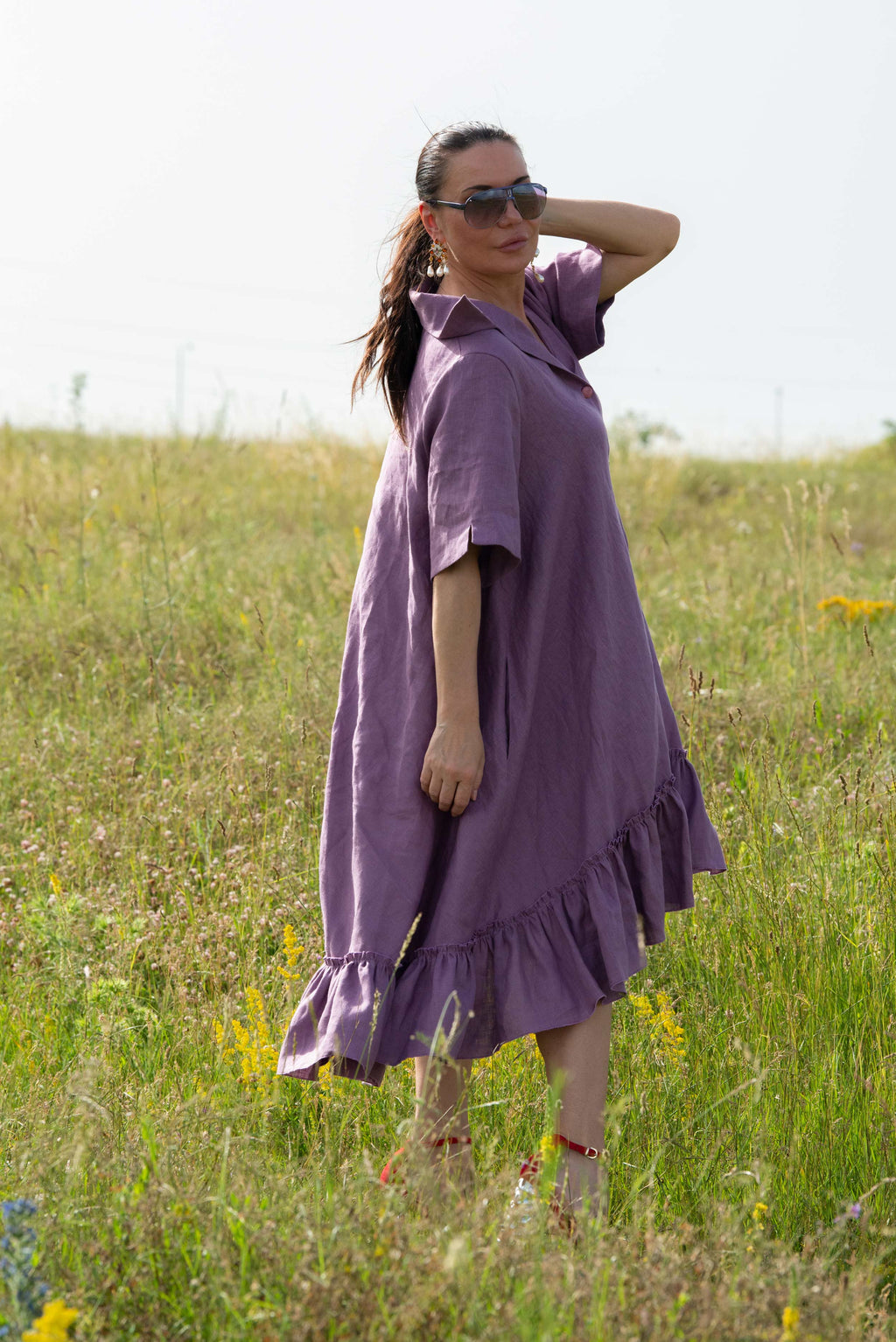 Woman in a purple dress standing in a grassy field with a clear sky.