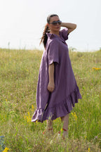 Woman in a purple dress standing in a grassy field with a clear sky.