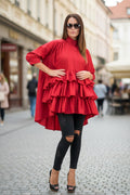 Woman wearing a red layered dress and black leggings on a street.
