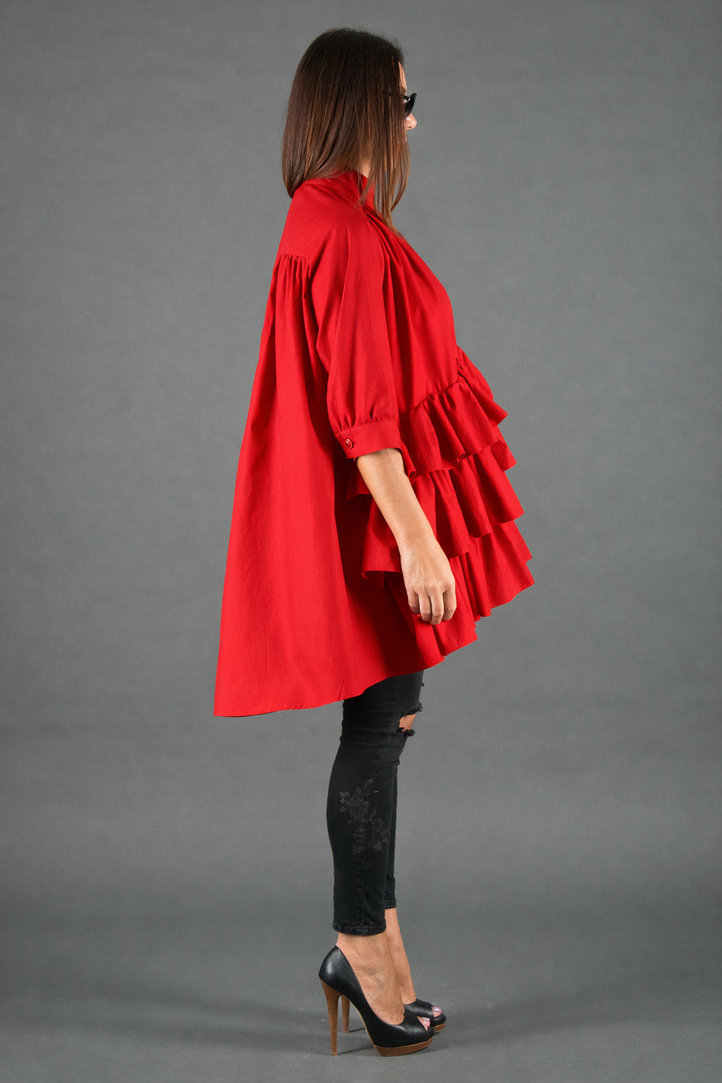 Woman wearing a red coat with ruffled layers on a gray background