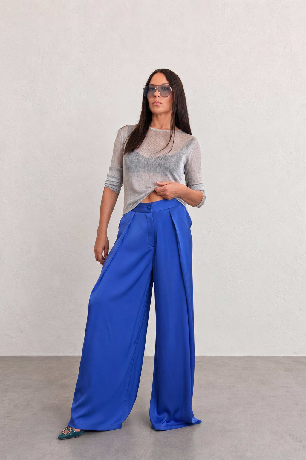 Woman wearing a gray top and blue wide-leg pants against a plain background
