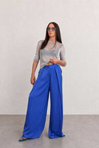 Woman wearing a gray top and blue wide-leg pants against a plain background