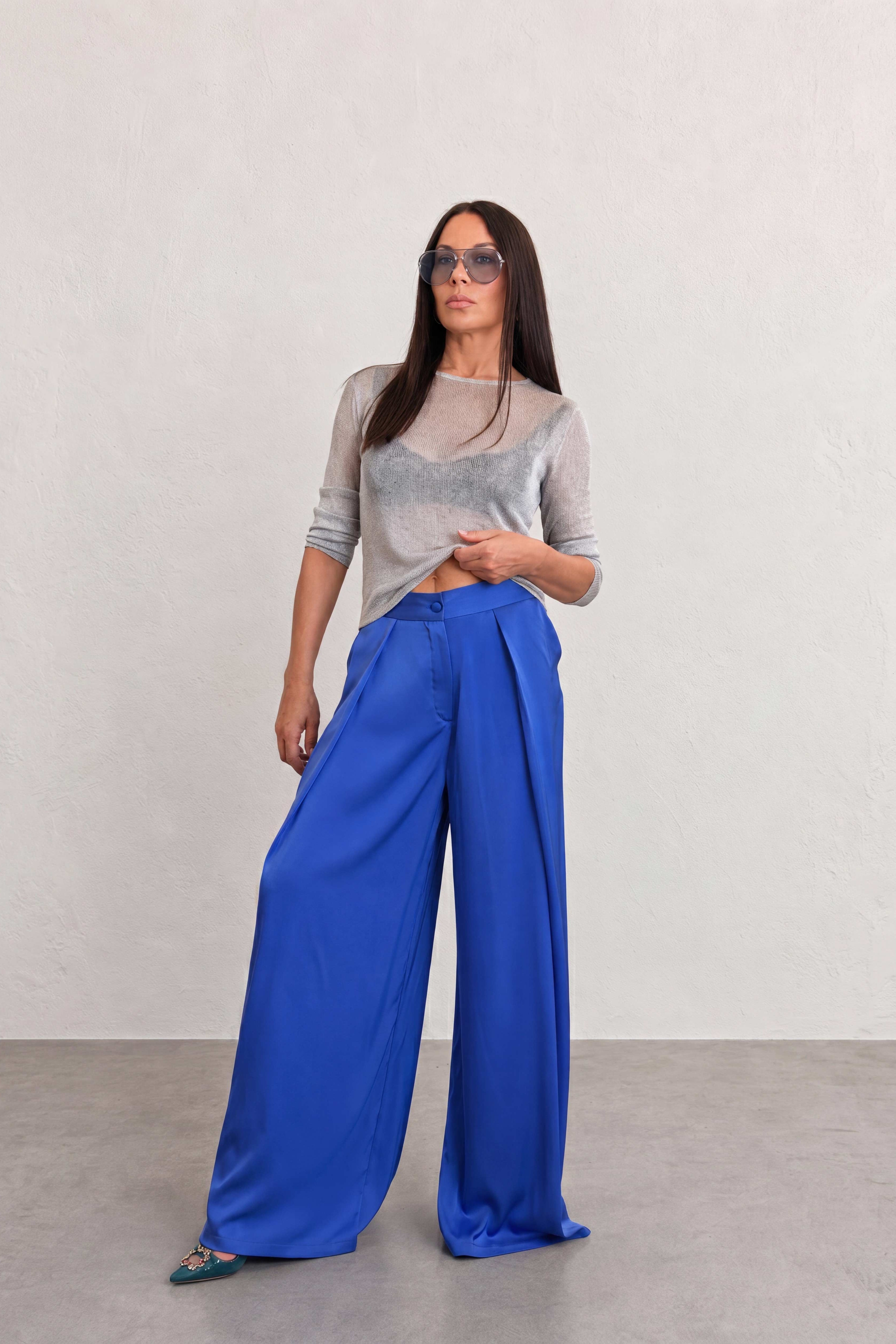 Woman wearing a gray top and blue wide-leg pants against a plain background