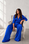 Woman in a blue jumpsuit sitting on a white chair in a bright room.