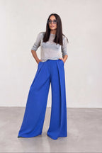 Woman wearing a gray sweater and blue wide-leg pants against a white background
