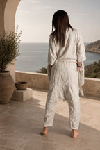 Person wearing a light-beige outfit standing on a stone patio with a scenic view of the ocean.