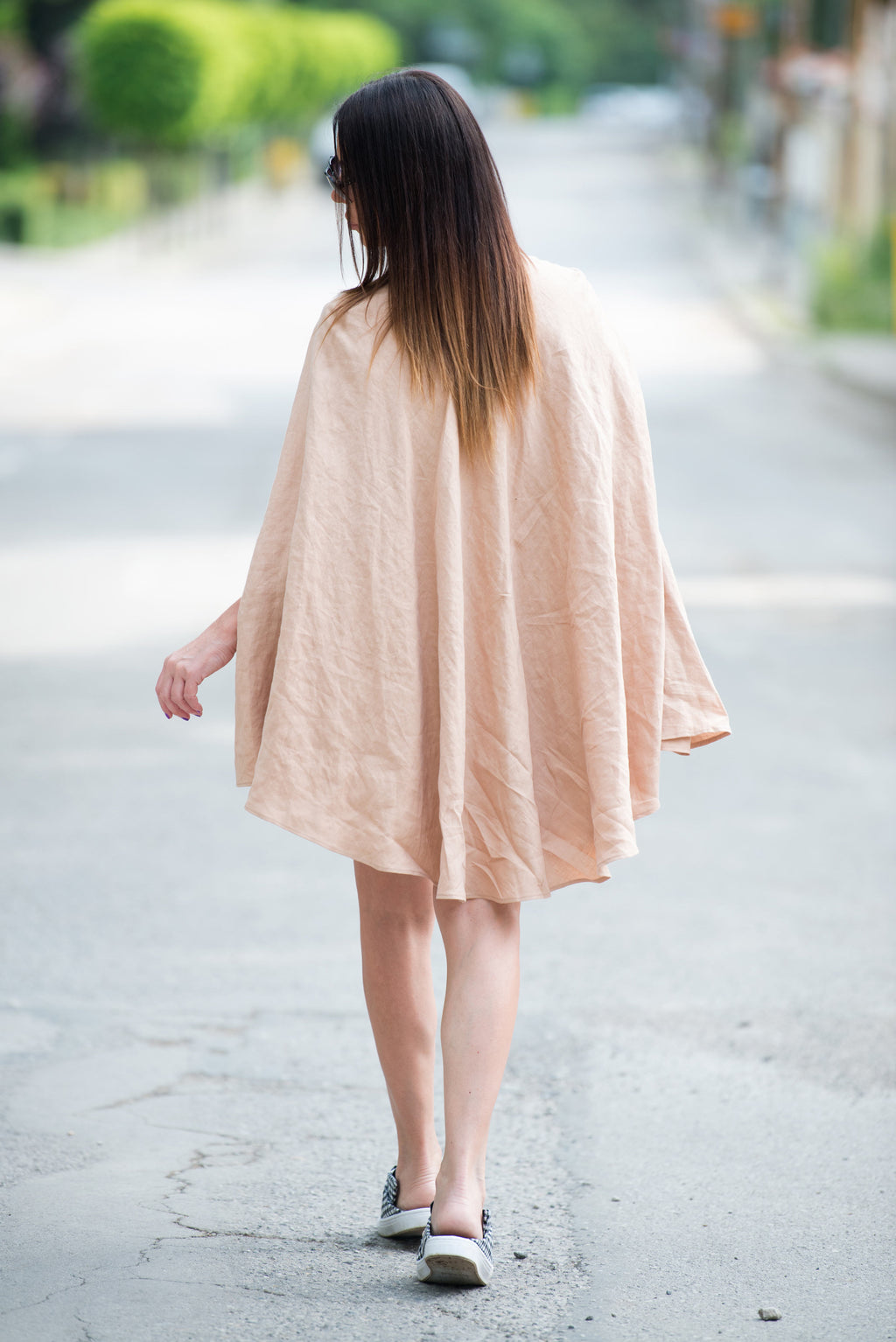 Woman walking on a road wearing a light beige linen cape dress 