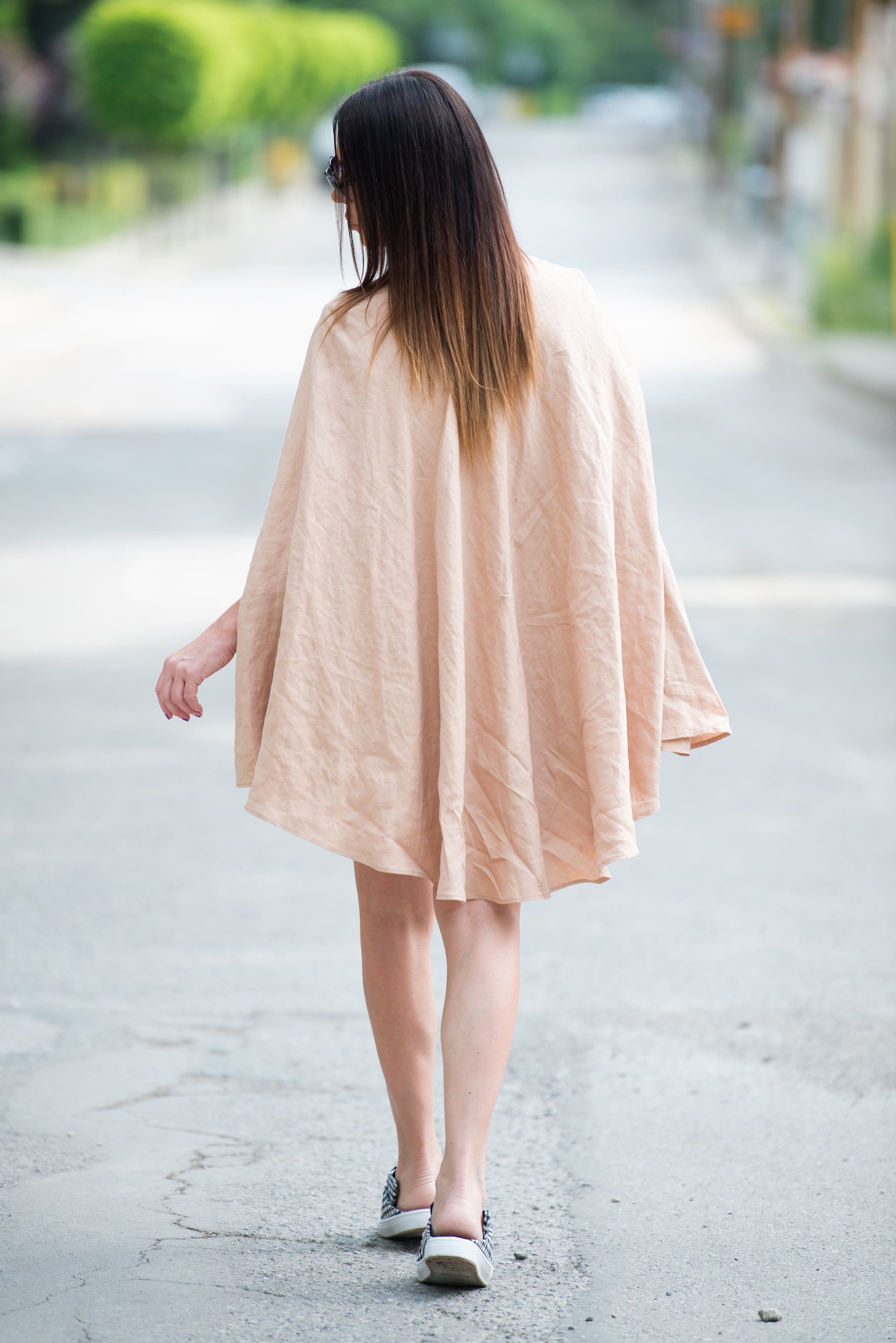 Woman walking on a road wearing a light beige linen cape dress 