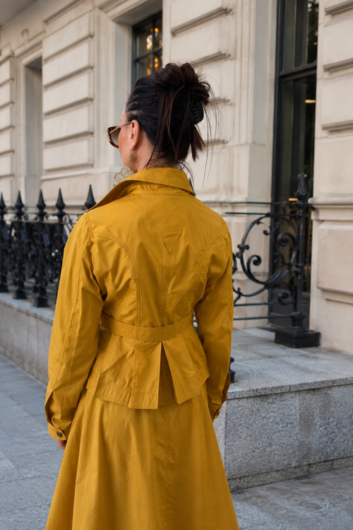Person wearing a yellow trench coat standing on a city street.