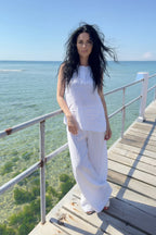 Woman in a white outfit standing on a wooden deck by the ocean.