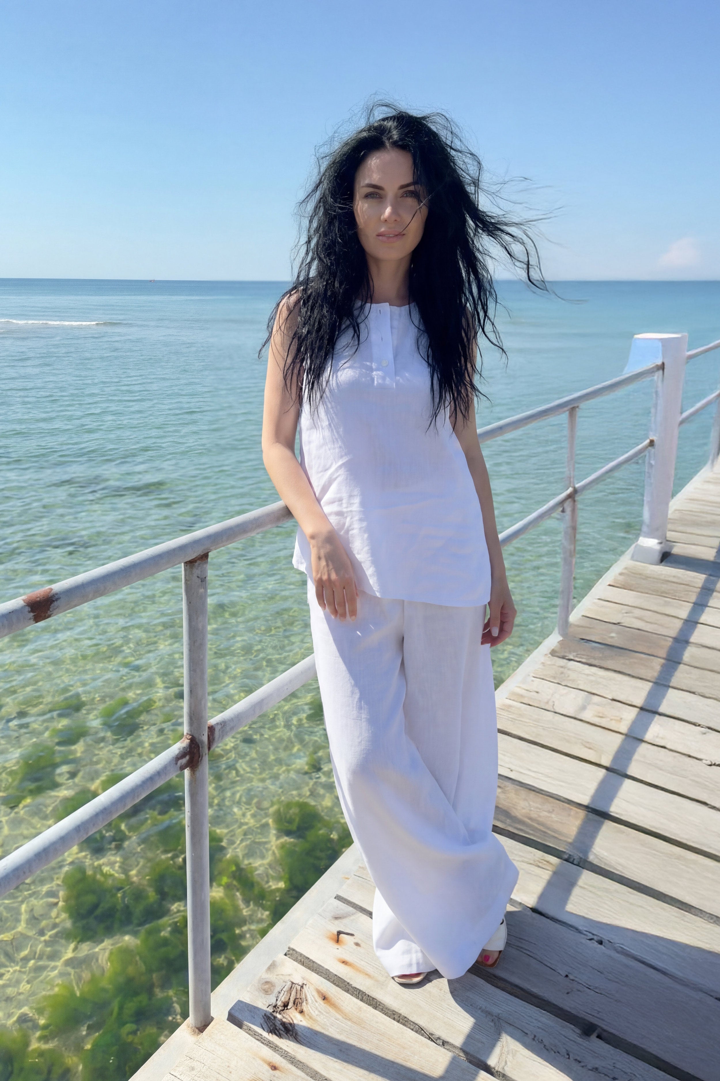 Woman in a white outfit standing on a wooden deck by the ocean.