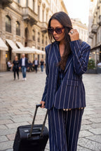 Woman in a blue pinstripe suit with sunglasses and a suitcase on a city street.