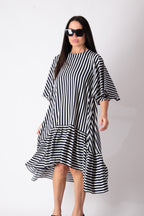 A woman modeling a black and white vertically striped midi dress with a ruffled hem and elbow-length sleeves, styled with black sunglasses against a plain white studio background.