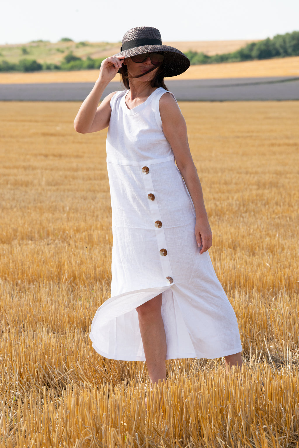 Woman in a white linen dress with buttons standing in a wheat field