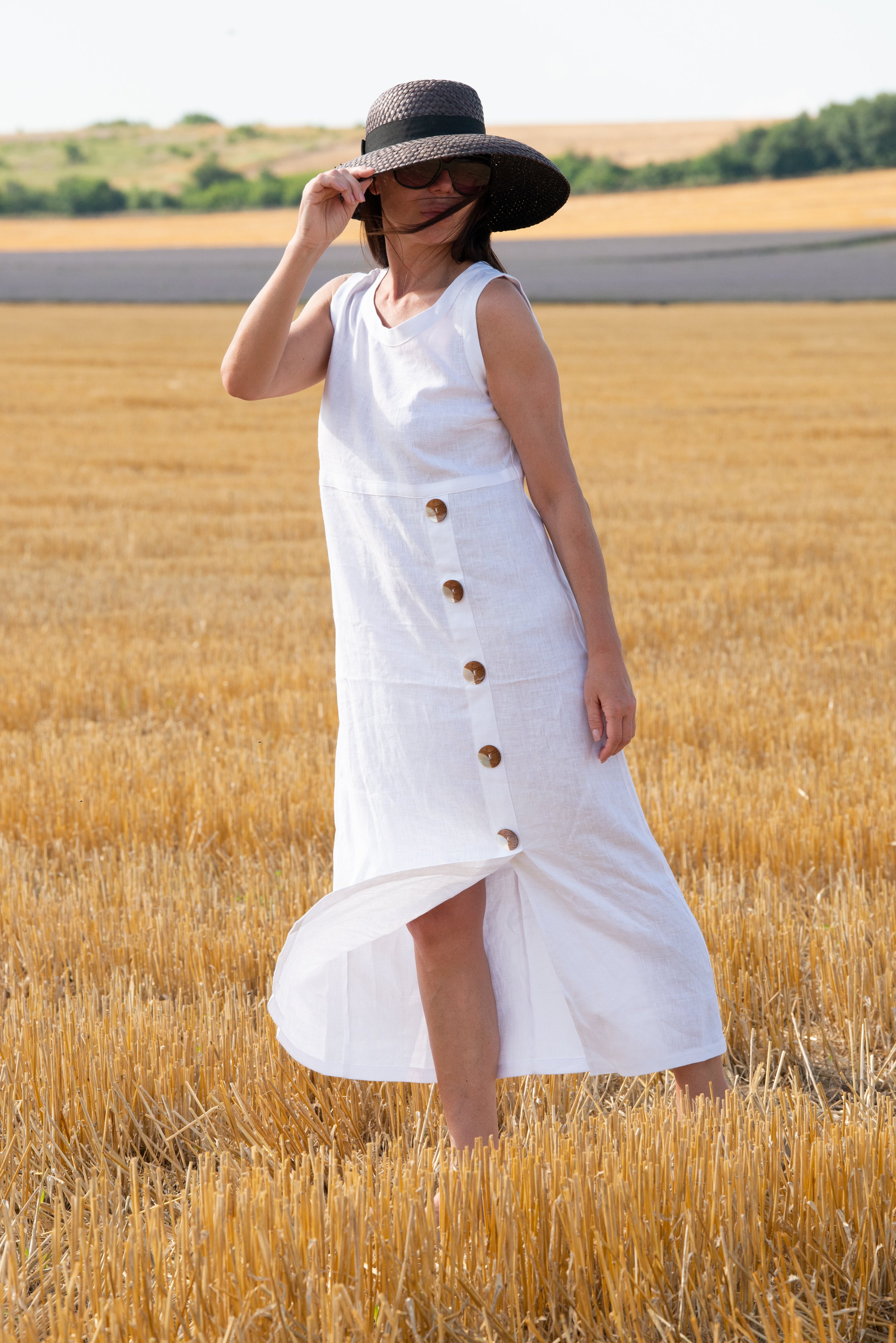 Woman in a white linen dress with buttons standing in a wheat field