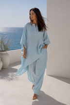Woman in light blue linen outfit standing on a sunlit terrace with ocean view