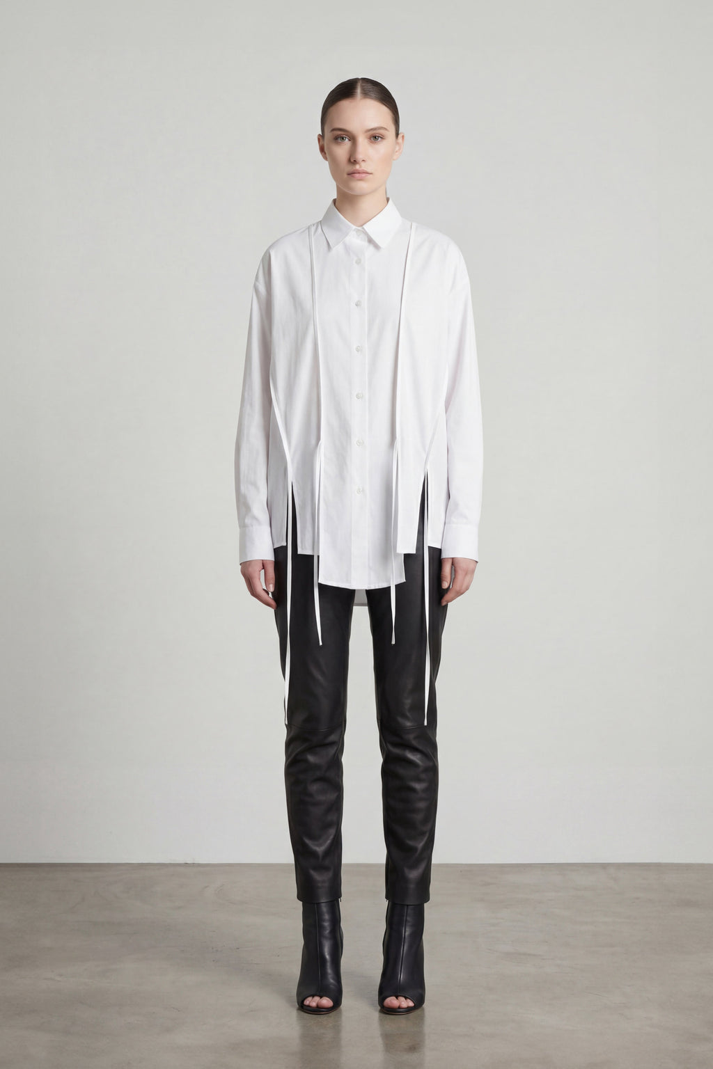 Person wearing a white shirt with a unique design and black pants on a plain background