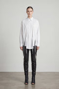 Person wearing a white shirt with a unique design and black pants on a plain background