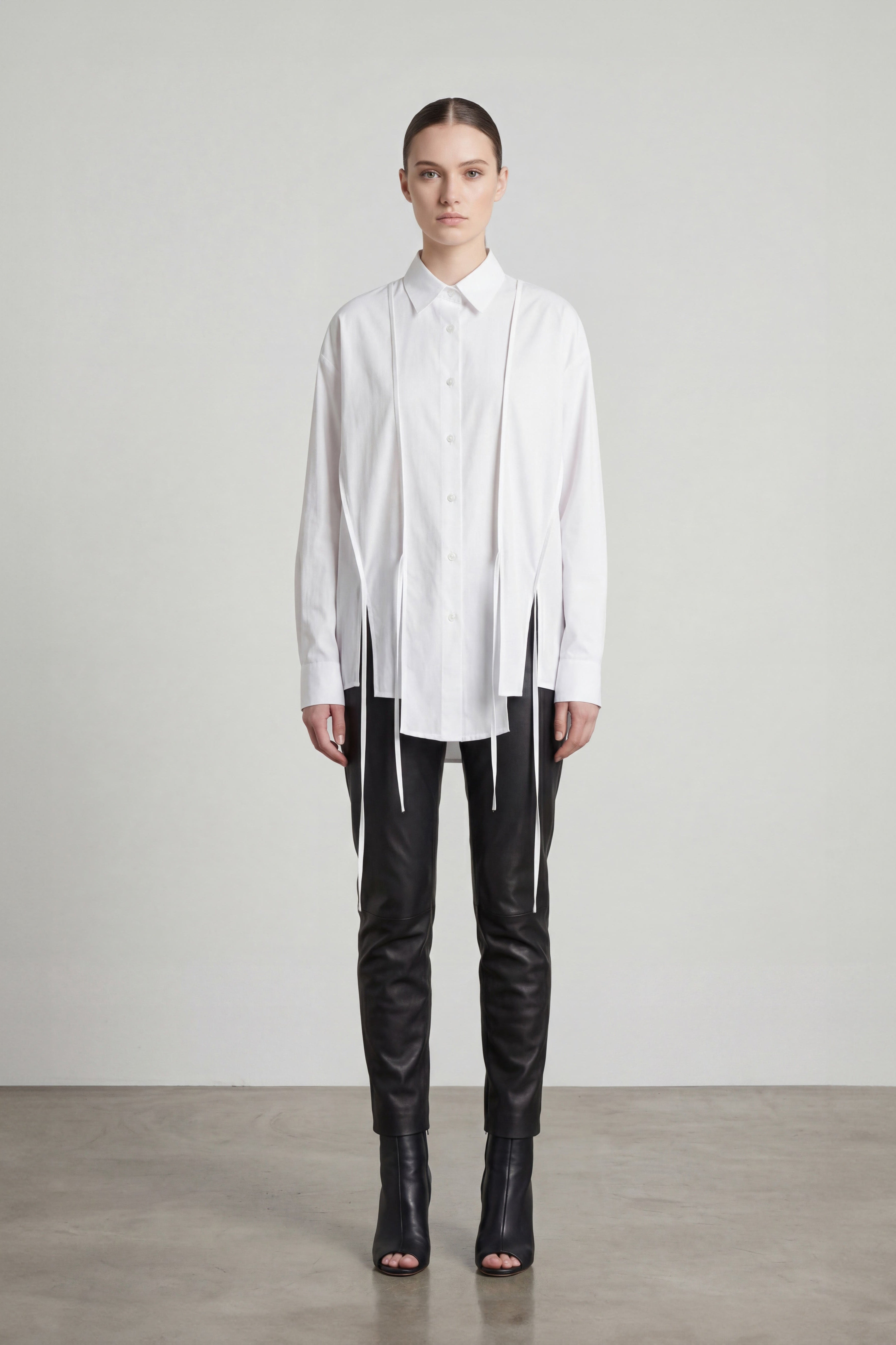Person wearing a white shirt with a unique design and black pants on a plain background