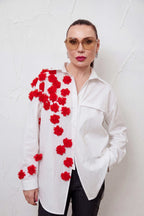 Person wearing a white shirt with red floral patterns against a textured white background
