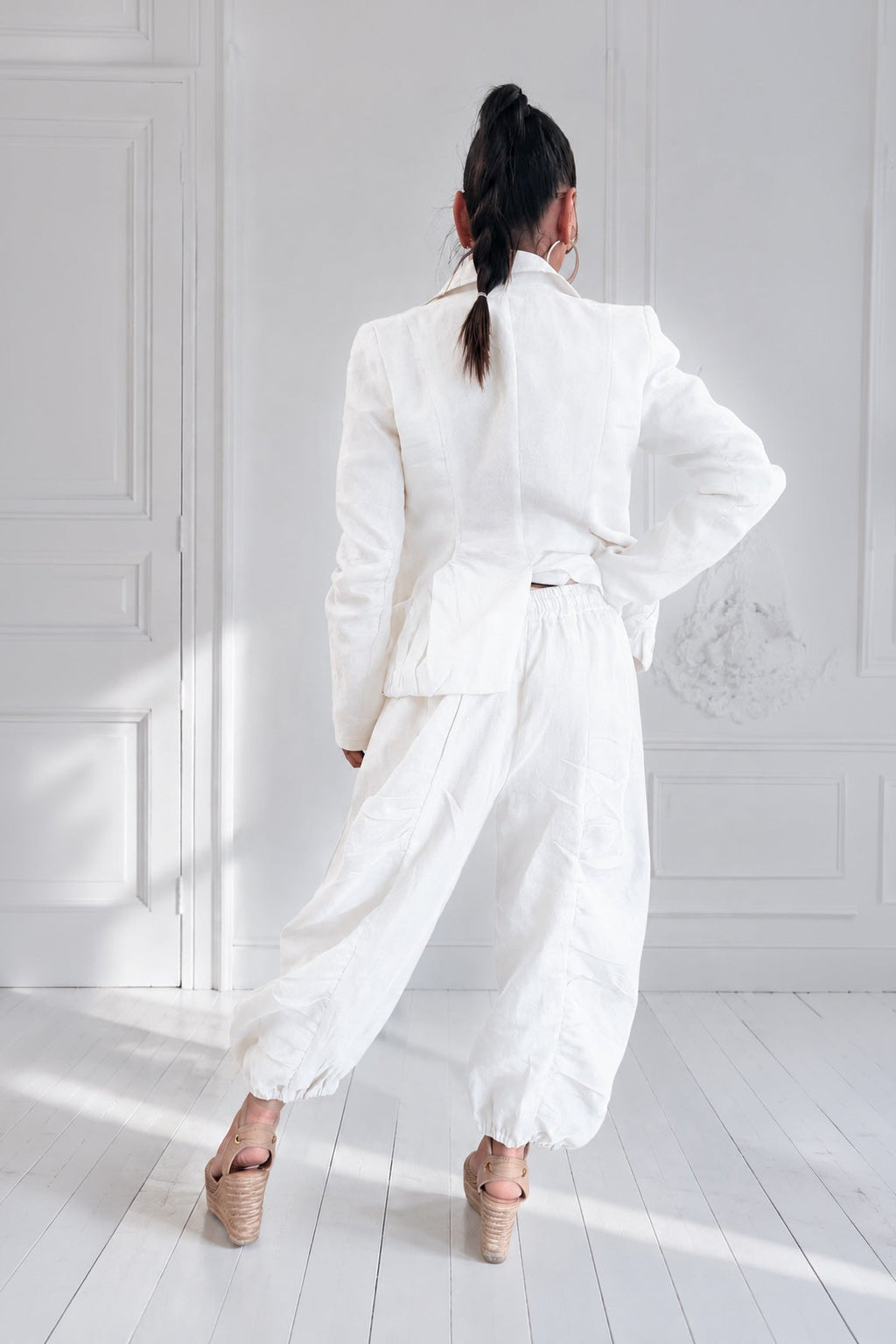 Person wearing a white outfit standing in a bright room with white walls and floor.