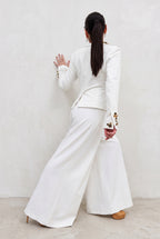 Person wearing a white outfit with floral embroidery, standing against a plain background