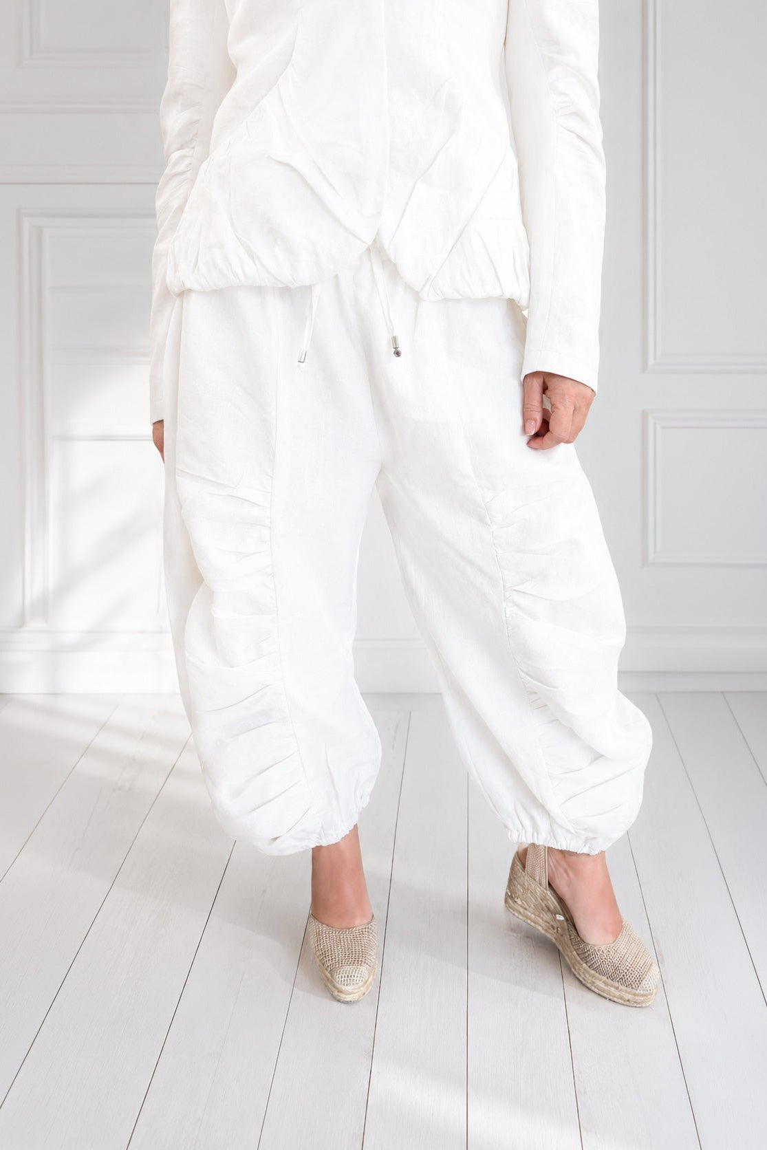 Person wearing a white outfit with wide-leg pants in a minimalistic room.