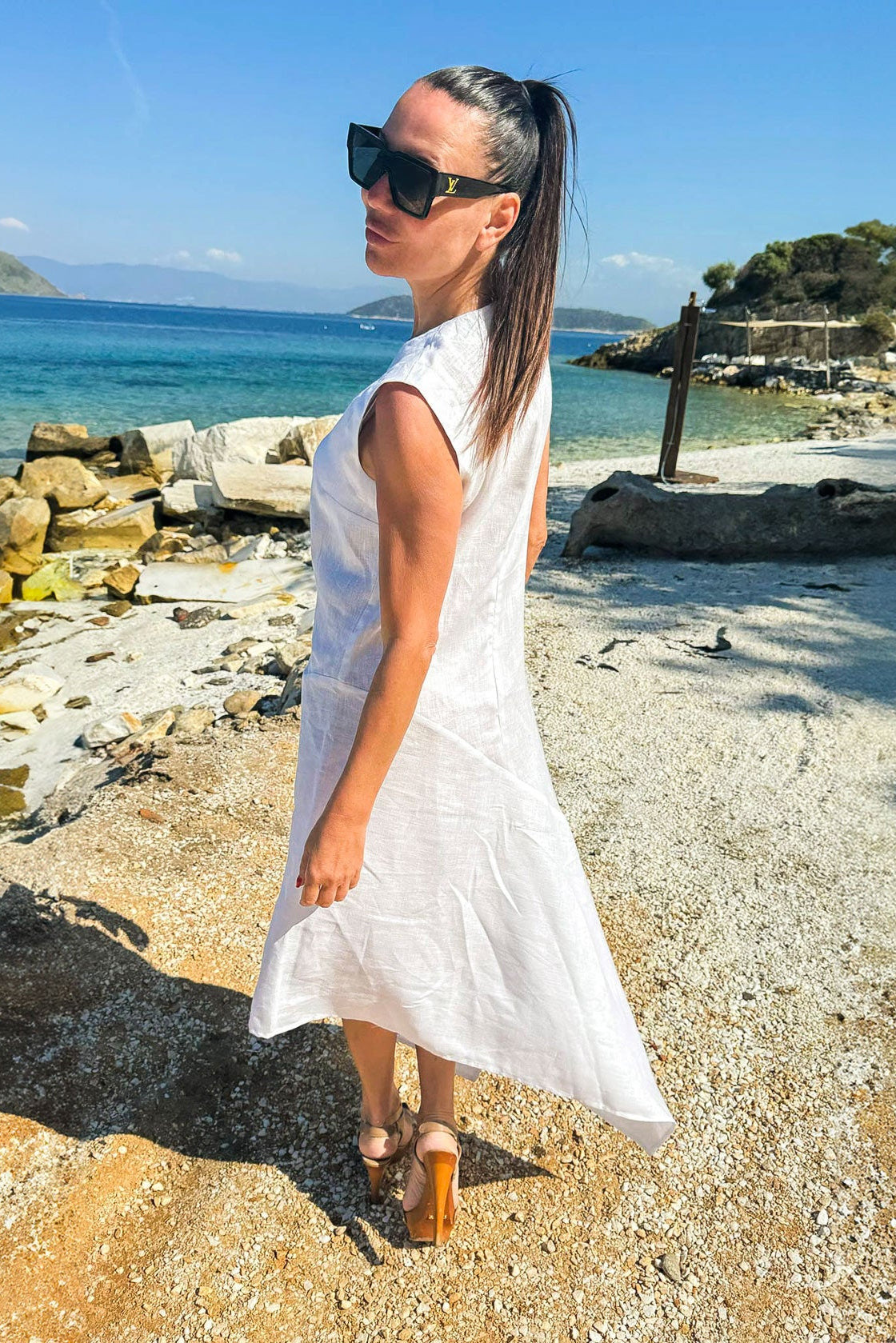 Woman in a white dress standing on a rocky beach with ocean and sky in the background