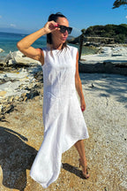 Woman in a white dress standing on a rocky beach with ocean and sky in the background