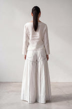 Person wearing a white outfit with wide-leg pants against a plain background