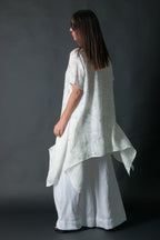 Woman wearing a white linen dress against a dark background