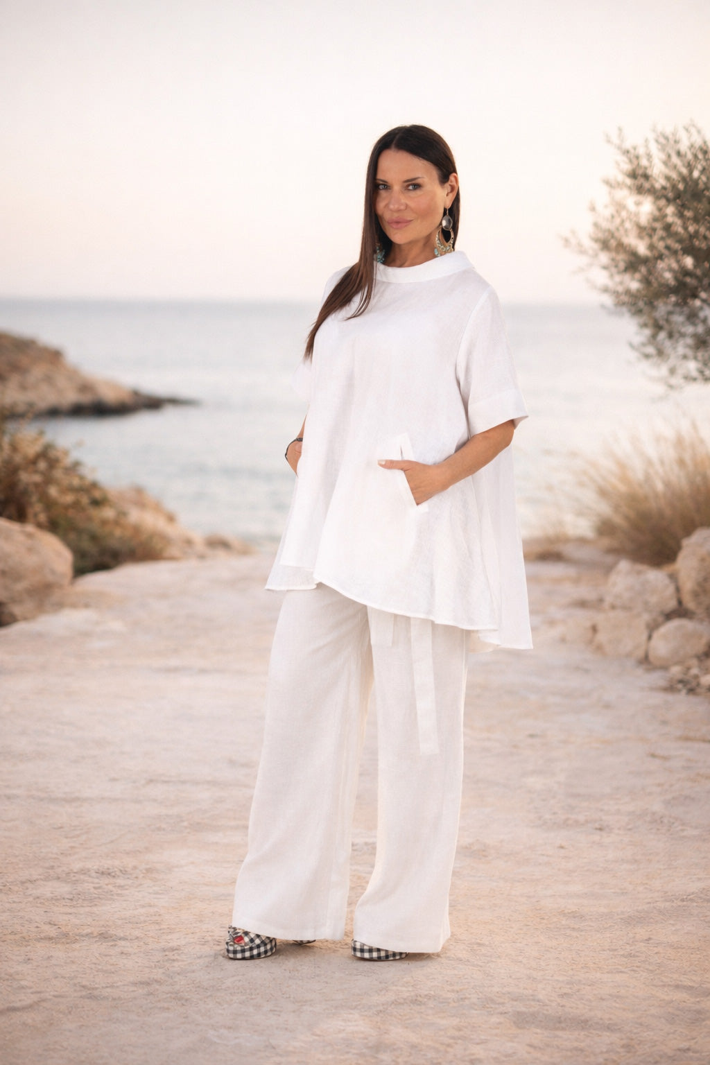 Woman in a white outfit standing by a scenic coastal area.