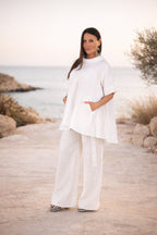 Woman in a white outfit standing by a scenic coastal area.