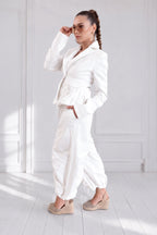 Woman in a white outfit standing in a bright room with white walls and floor.
