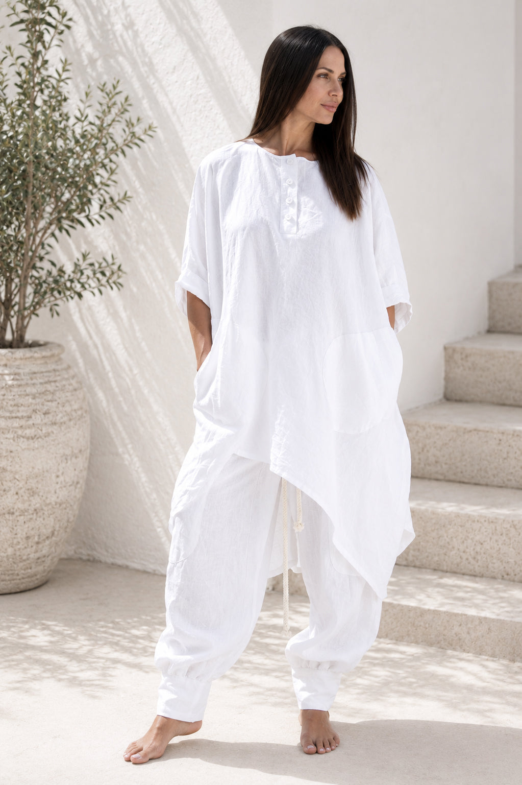Woman wearing a white linen outfit in a minimalistic setting with a plant and stairs.