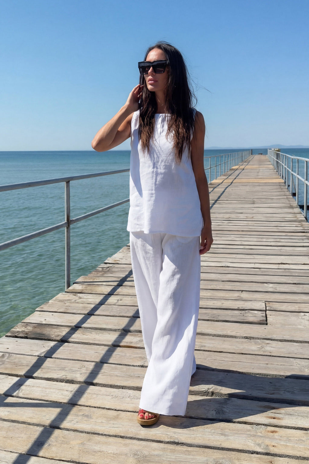 Woman in a white outfit standing on a wooden pier by the ocean