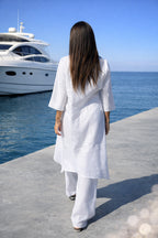 Woman in a white outfit walking on a dock with a yacht in the background