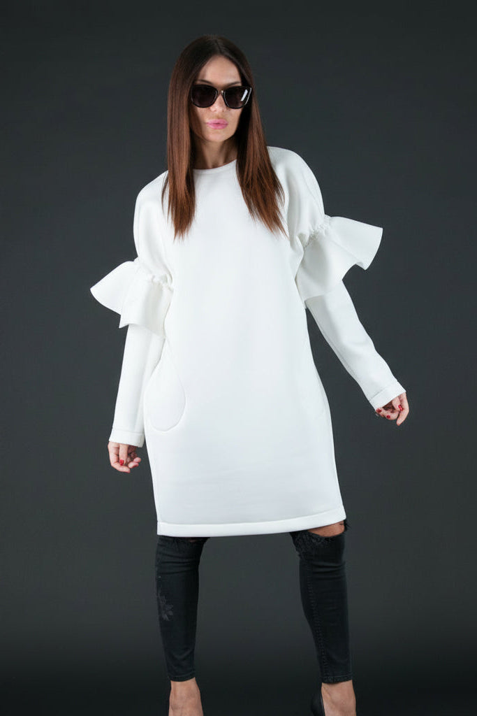 Woman wearing a white dress with ruffled sleeves against a dark background