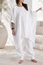 Person wearing a loose-fitting white linen outfit in a bright, minimalistic setting.