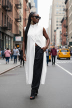 Woman in a white sleeveless top and black pants walking on a city street.