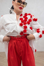 Person wearing a white blouse with red floral patterns and red pants against a plain background