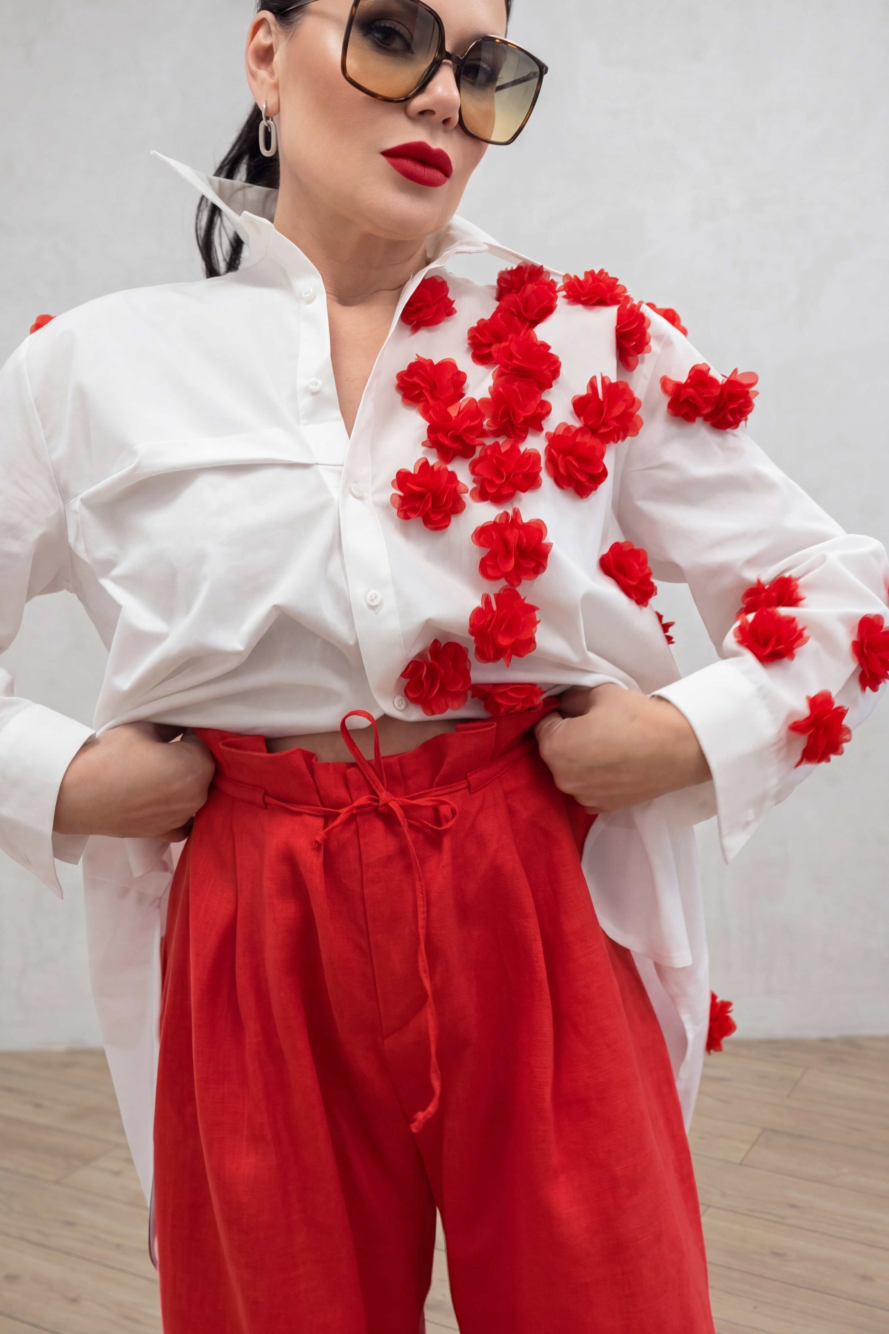 Person wearing a white blouse with red floral patterns and red pants against a plain background