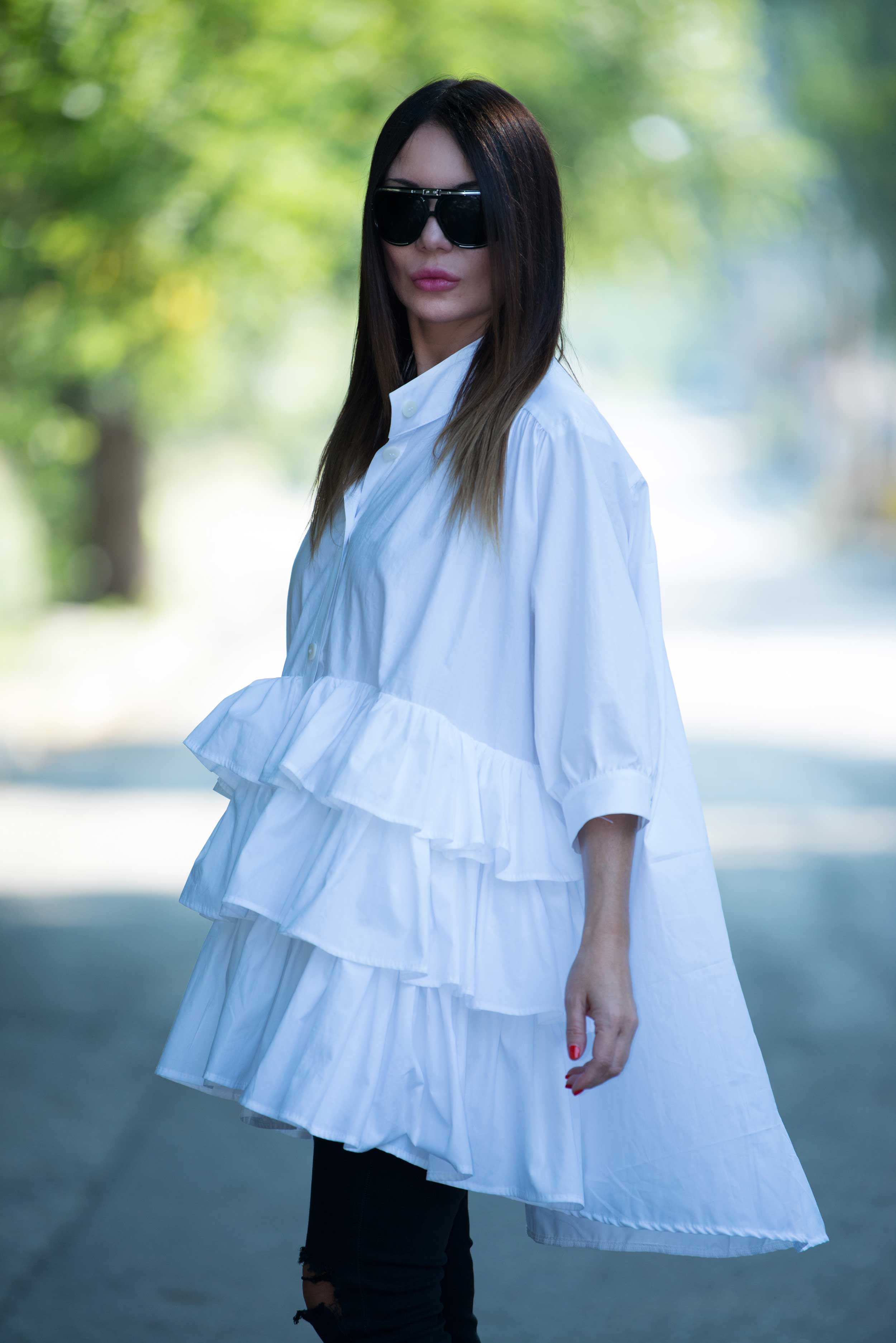 Woman wearing a white ruffled blouse with sunglasses outdoors.