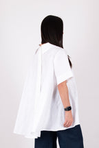 Person wearing a white blouse with cut-out shoulders on a plain background