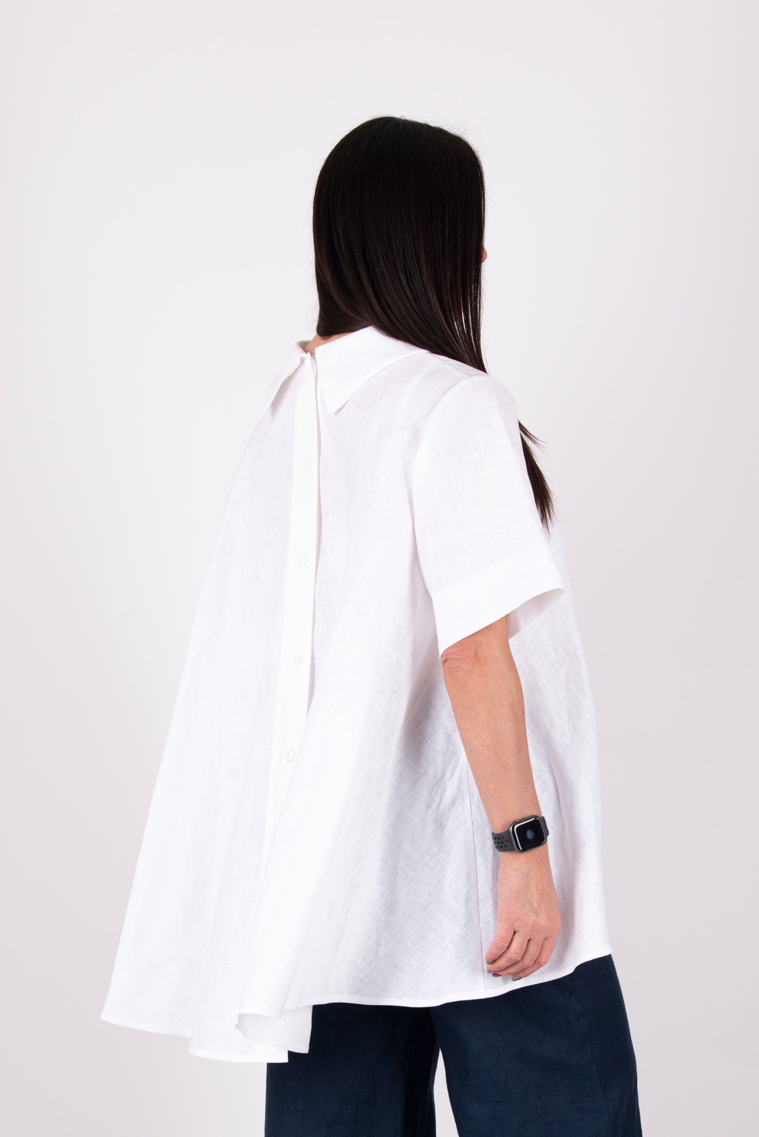 Person wearing a white blouse with cut-out shoulders on a plain background