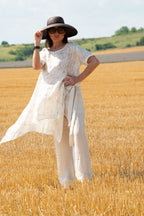 Woman in a white dress and black hat standing in a field of golden wheat.